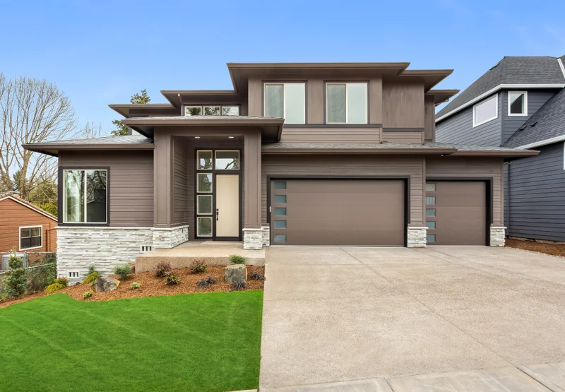 Contemporary two-storey home with taupe siding, stone accents, a three-car garage and a wide concrete driveway