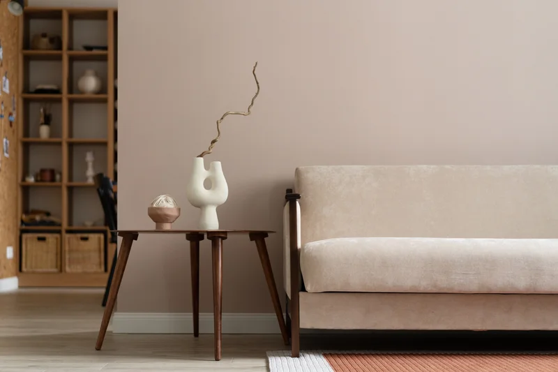 Minimal living room with a cream sofa, walnut side table, sculptural white vase and warm beige walls