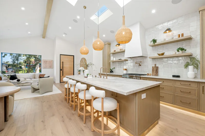 Vaulted penthouse kitchen with skylights, a long oak island with white stools and rattan pendant lights