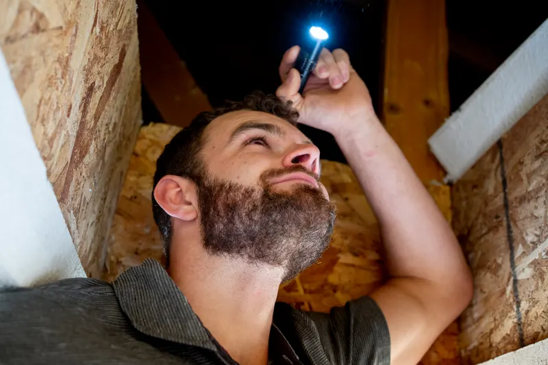 Inspector shining a flashlight across attic framing and sheathing during a home inspection