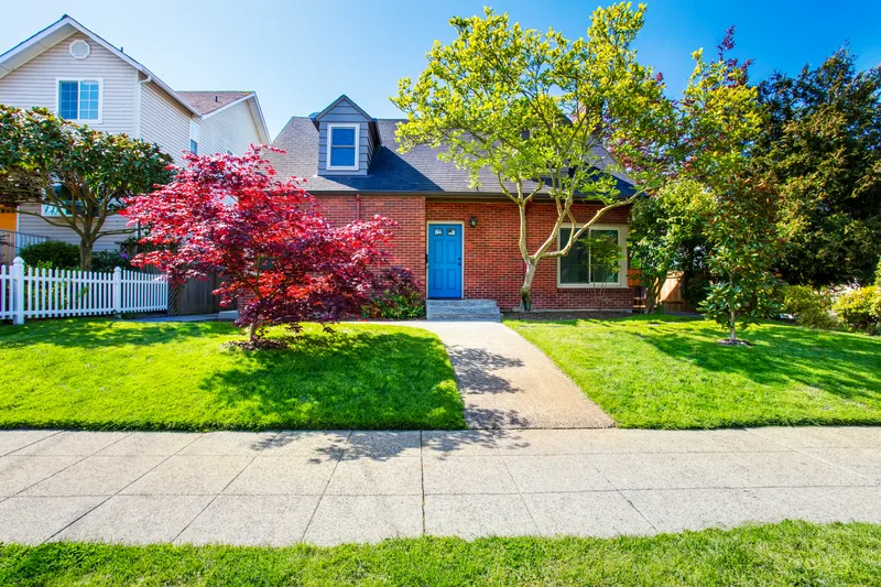A red brick family home with a blue front door, a red maple and a white picket fence