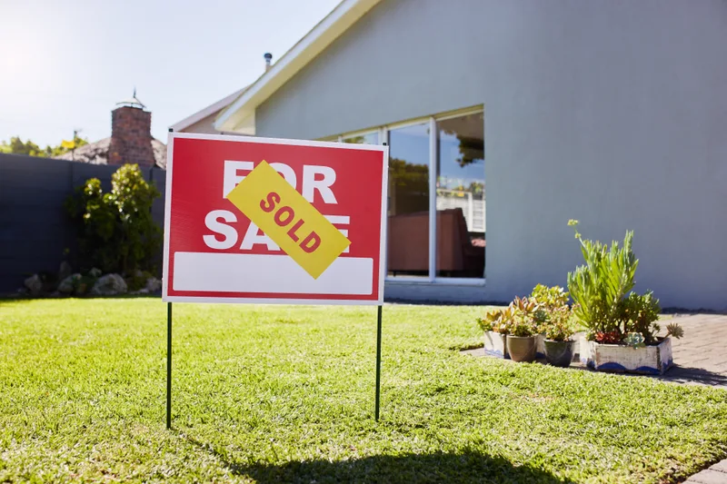 A for-sale sign with a yellow sold rider on the front lawn of a renovated house