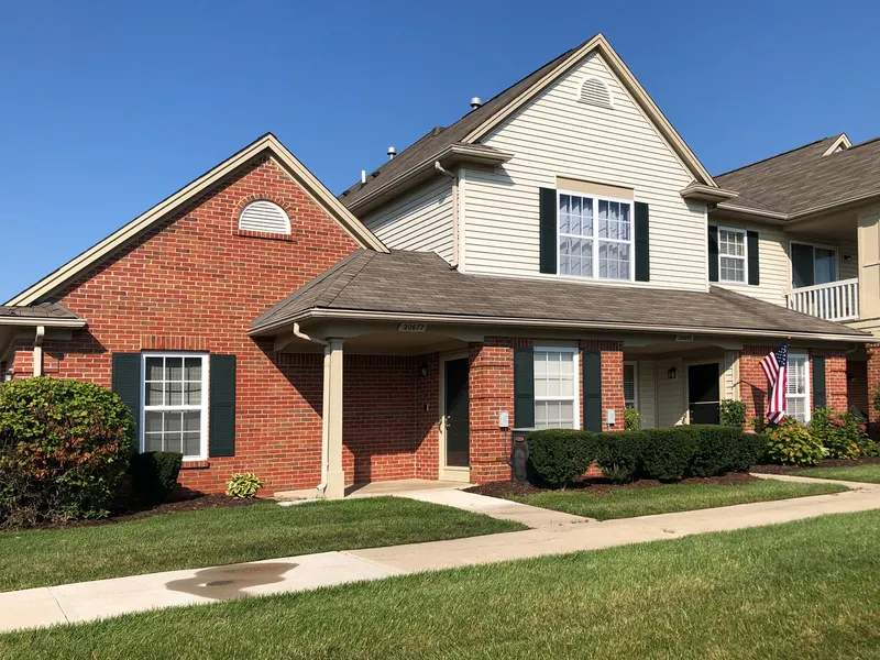 Brick townhome-style building with covered entry porches, dark shutters and landscaped front beds on a sunny day