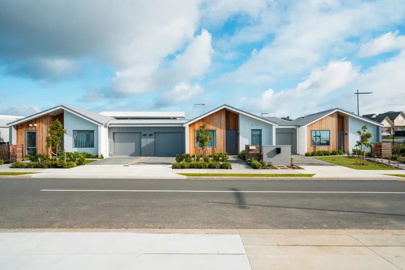 Street-front row of three tidy single-storey rental homes with grey siding, cedar accents and young landscaped yards