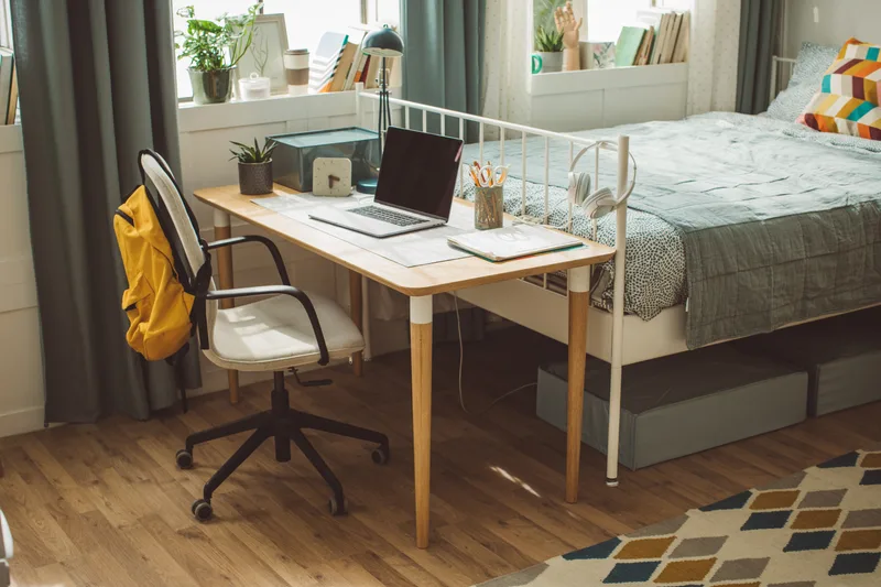 Tidy student dorm room with a desk, chair and made bed