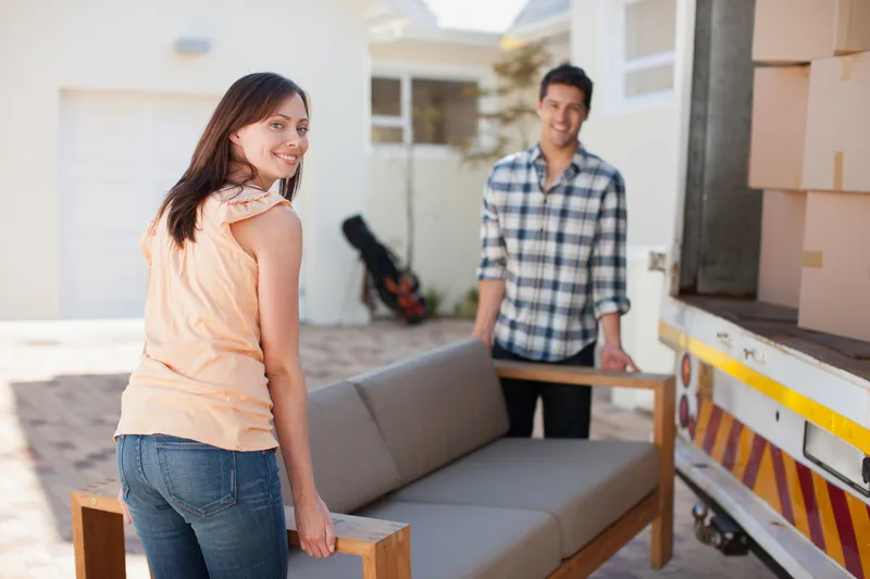 Couple carrying a gray sofa from a moving truck on a sunny day