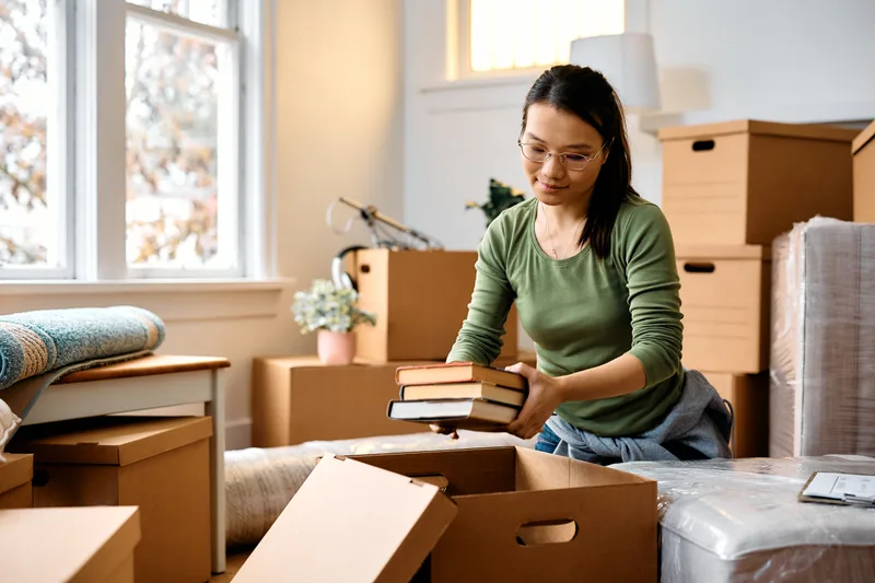 Woman lifting a stack of books out of a cardboard box among packed boxes