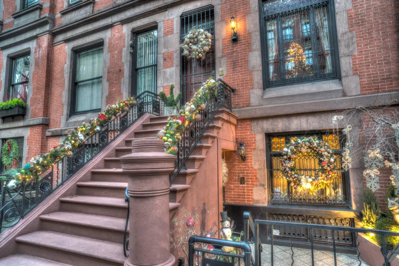 Brick townhouse stoop at No. 12 Bellamy Street dressed in evergreen garland and warm lantern light for its winter launch