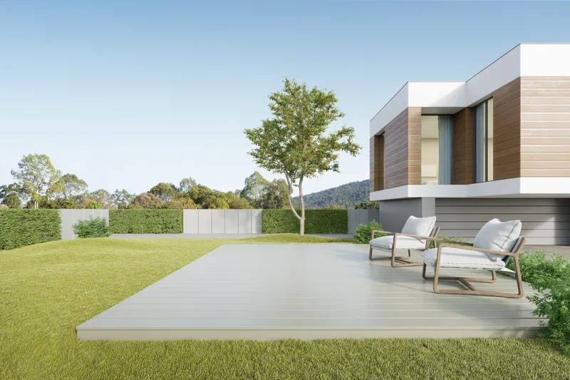 Vale House — a cantilevered timber-and-white volume behind a broad lawn, two lounge chairs on the pale deck under an open sky