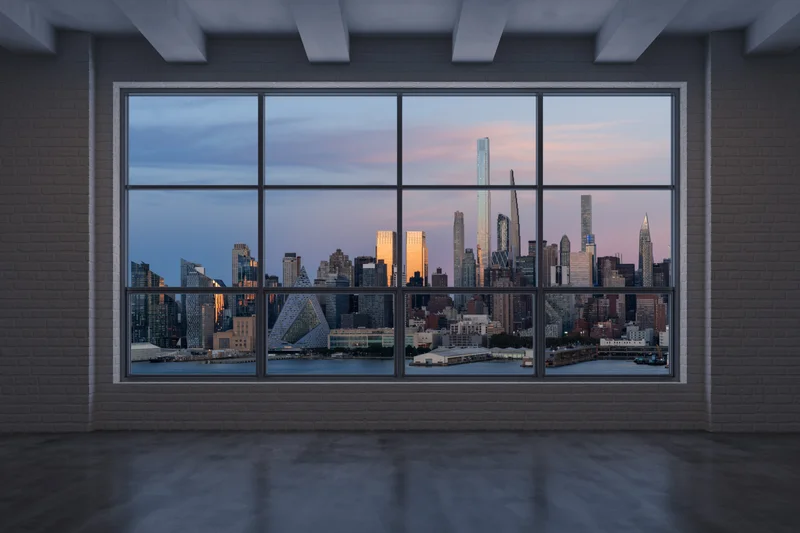 The Skyhall Loft's empty main hall — white brick, coffered concrete ceiling, and a sixteen-pane steel window filled with the skyline at sunset