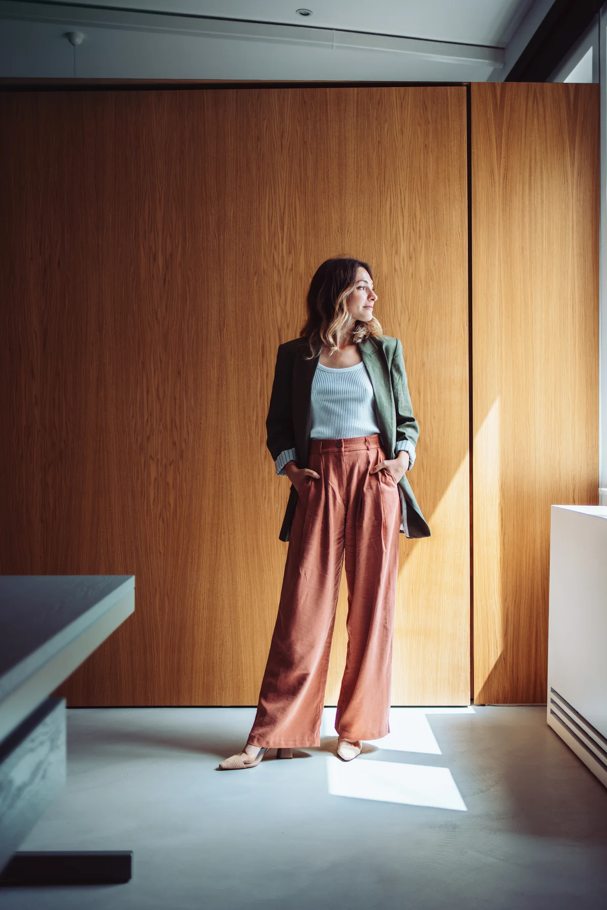 Olivia Voss standing against a warm oak-paneled wall, looking toward the window light