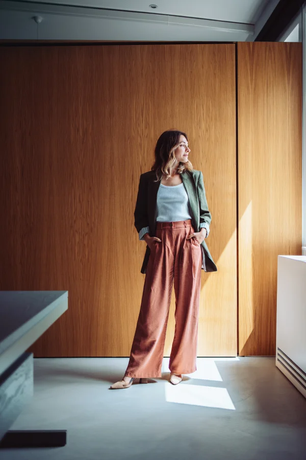 Olivia Voss standing against a warm oak-paneled wall, looking toward the window light