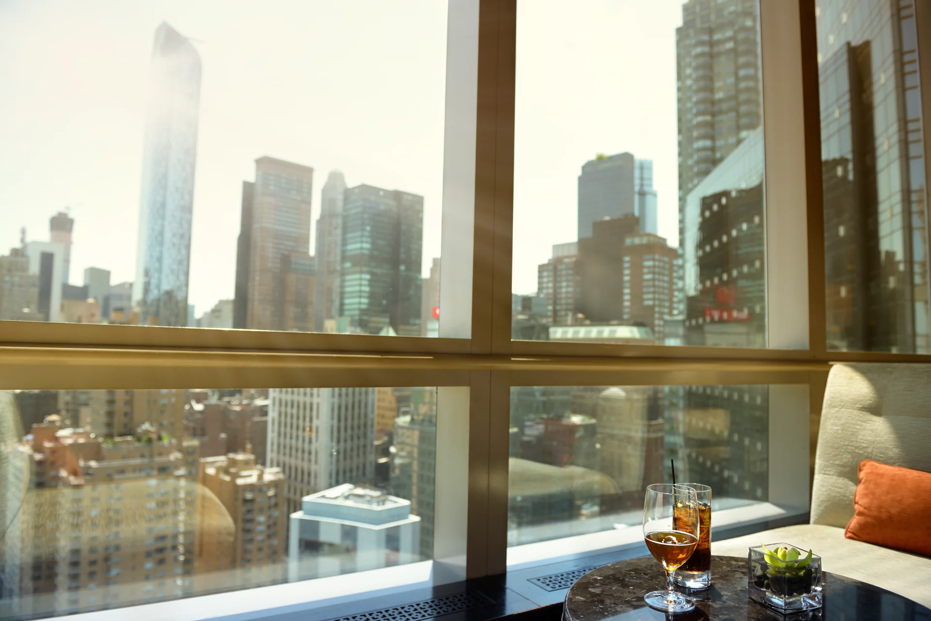 Late golden light raking through a tower window across the Alderport skyline, two glasses catching the sun on a marble table