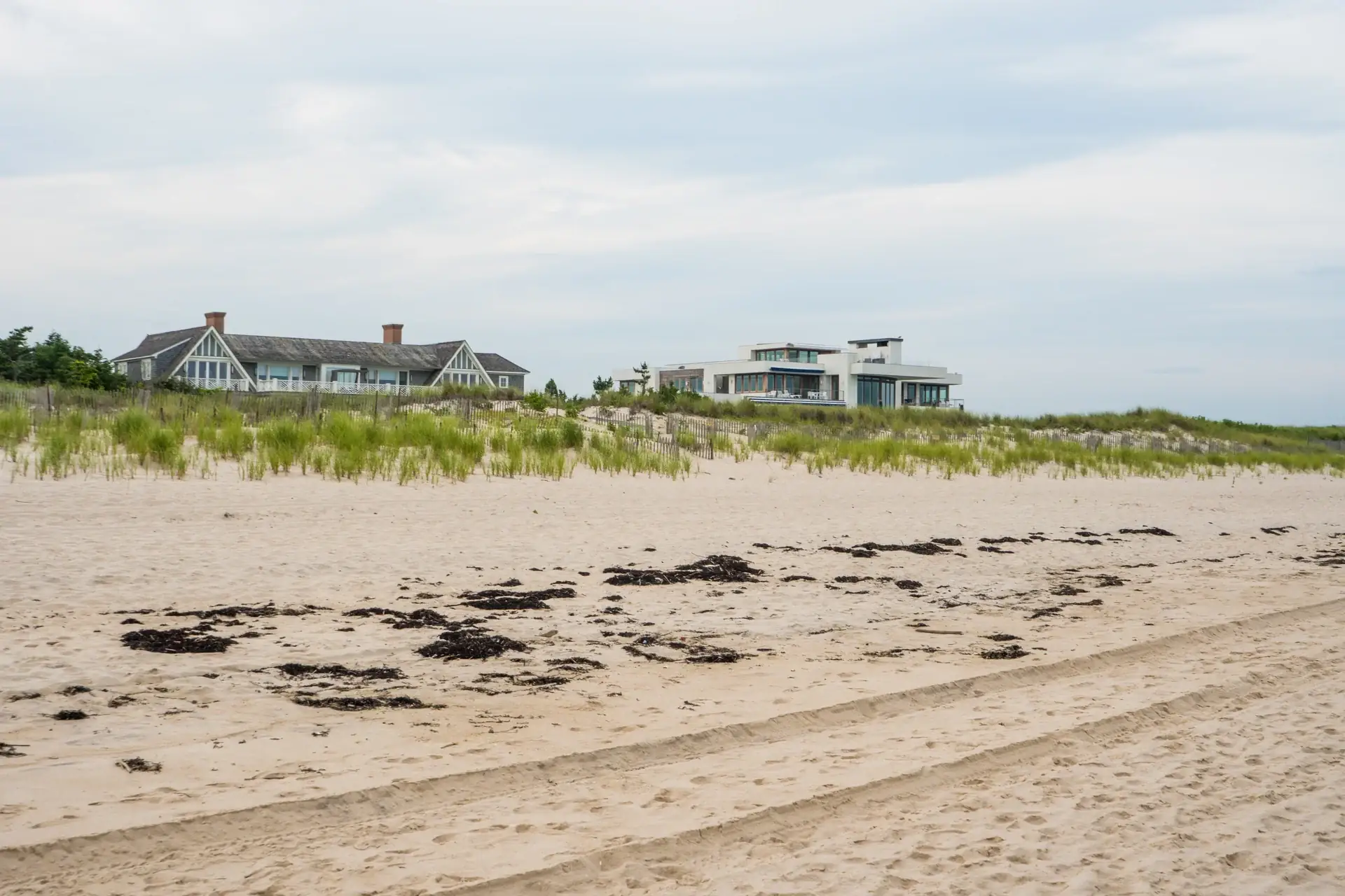 The Shingle House's twin-gabled silhouette above the dune grass, its modern white neighbor visible down the empty beach
