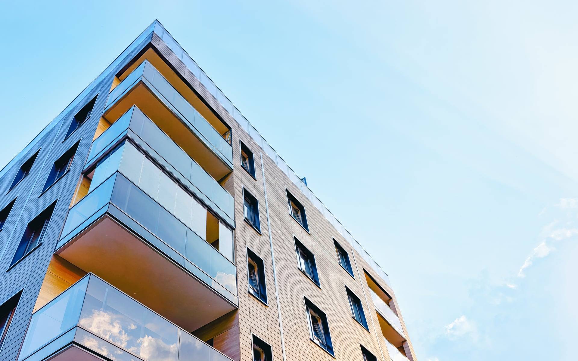 Low-angle view of a mid-rise condominium corner with glass balconies and warm timber-toned cladding under a clear sky — artist's impression of The Westwind.