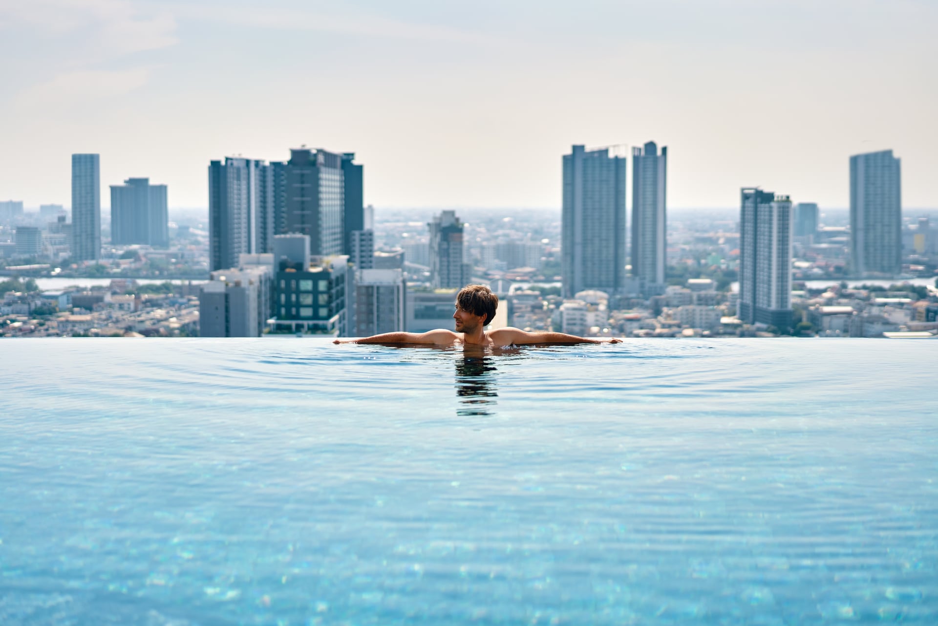 Swimmer resting arms along the infinity edge of the Horizon Pool, the whole city skyline laid out beyond — artist's impression.