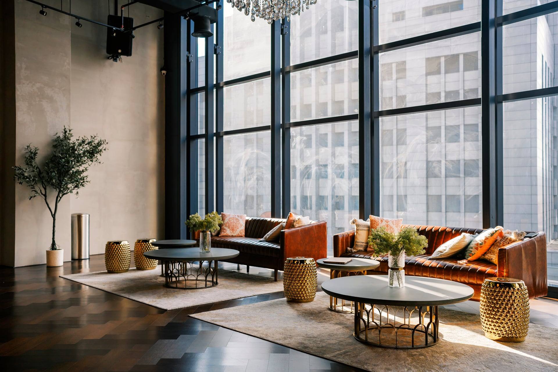 Double-height residents' lounge with black-framed glazing, tan leather sofas and brass drum tables — artist's impression.