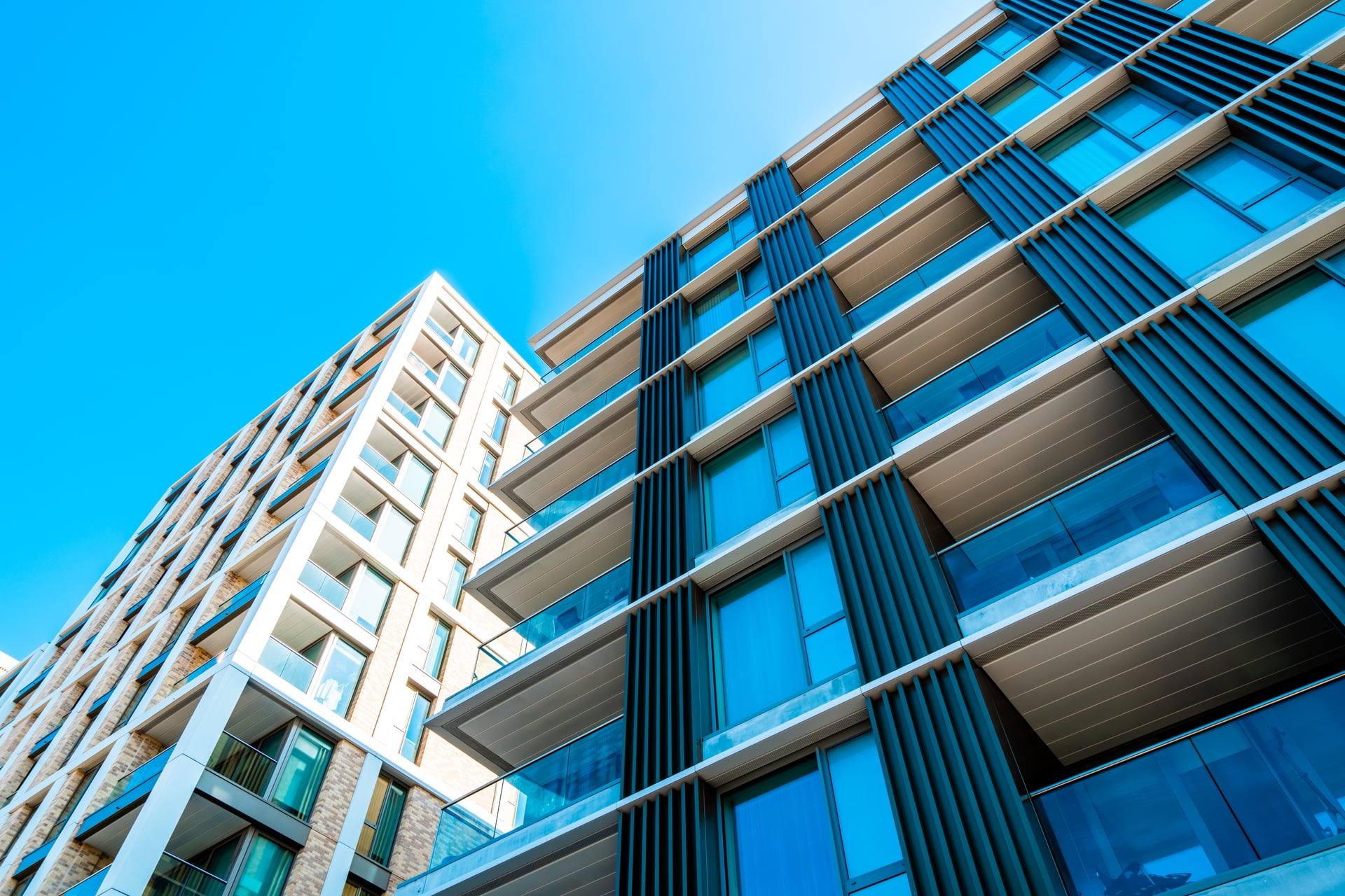 Two modern condominium towers seen from below, glass balconies and dark vertical fins against a deep blue sky — artist's impression of The Westwind.