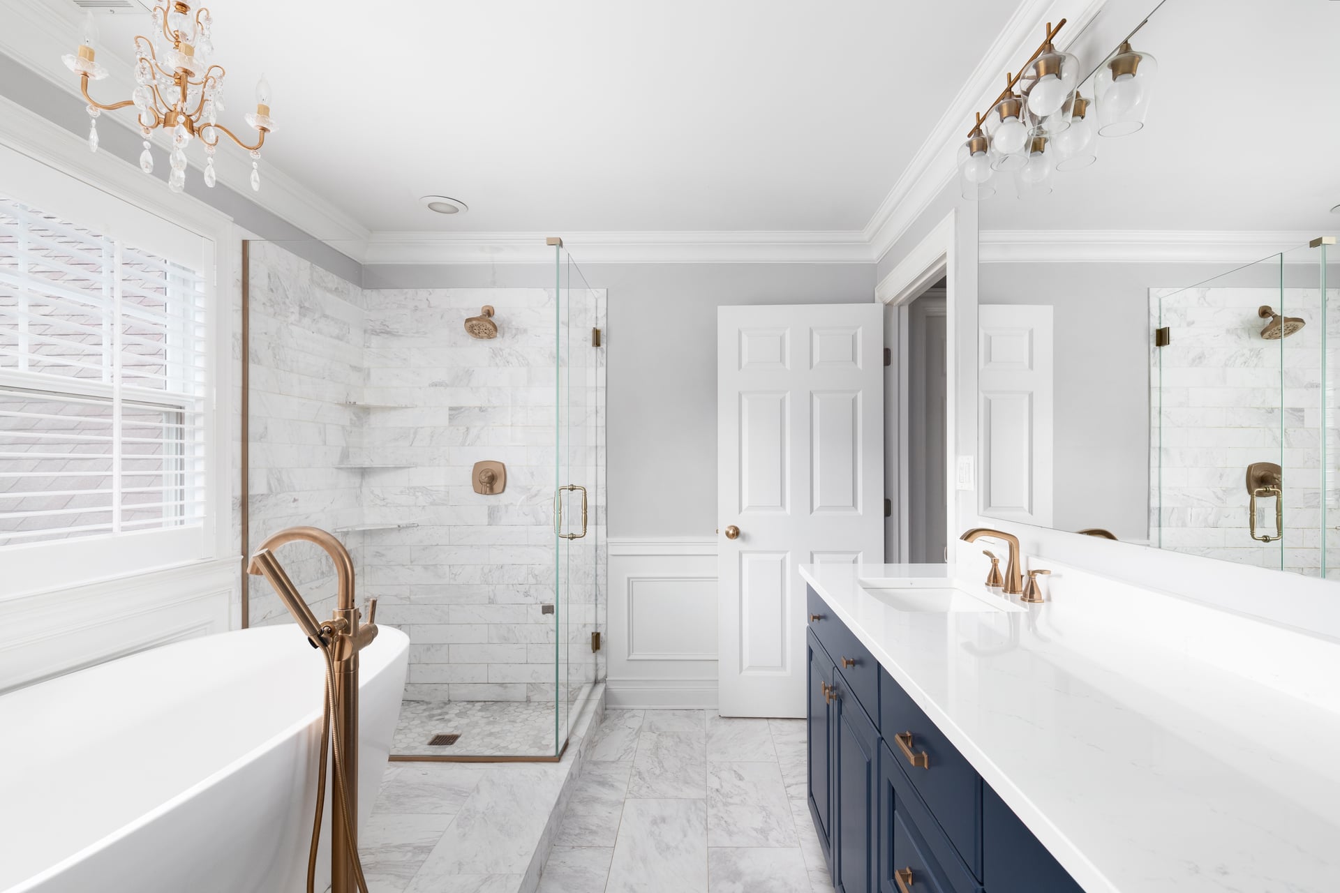 Meridian palette ensuite: marble-look shower surround and floor, freestanding tub with a floor-mounted brass filler, and a navy double vanity under brass sconces — artist's impression.
