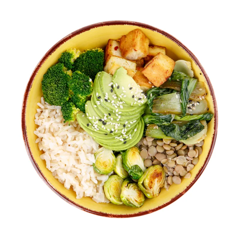 The Harvest Crunch bowl from above: fanned avocado, roasted broccoli, crispy brussels sprouts, tofu, lentils, and brown rice in a yellow bowl