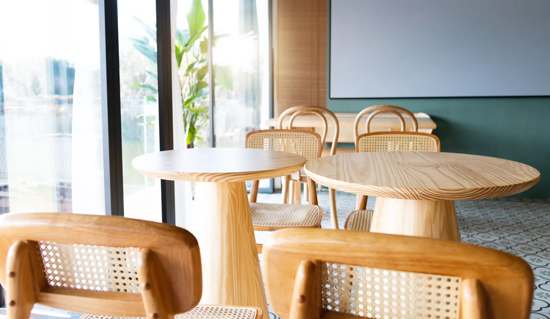 Bright Bowl & Branch dining room with pale wood tables, cane-back chairs, and a deep green feature wall