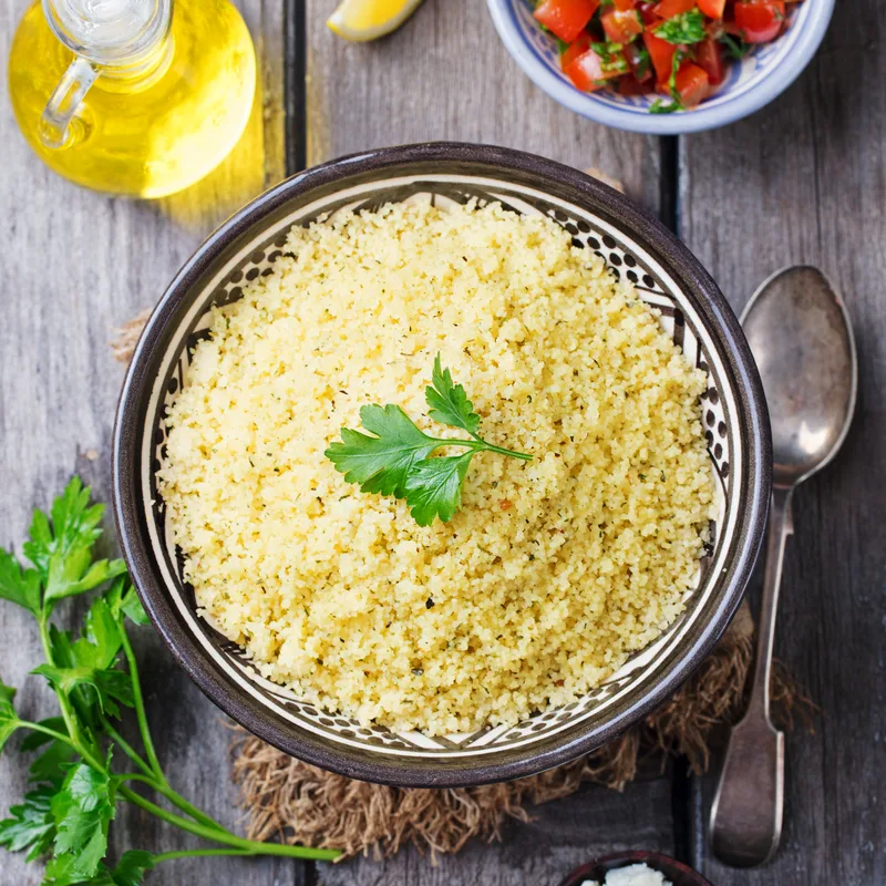 Bowl of lemon-herb couscous garnished with parsley, the base of the Sunset Harissa bowl