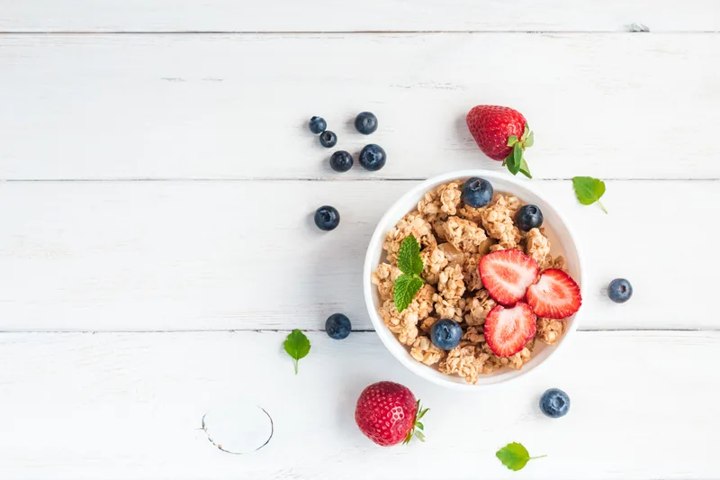 Morning Grove breakfast bowl of granola, strawberries, and blueberries on a white wood table