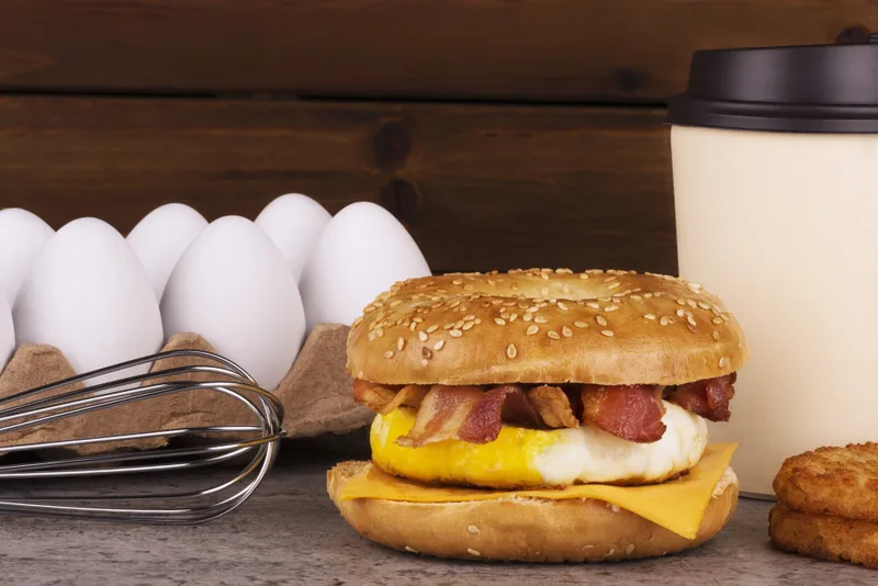 An egg, bacon and cheddar breakfast sandwich beside a takeaway coffee cup