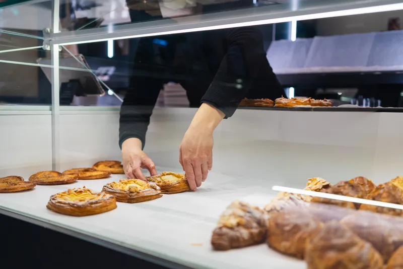A baker setting fresh pastries into a glass display case