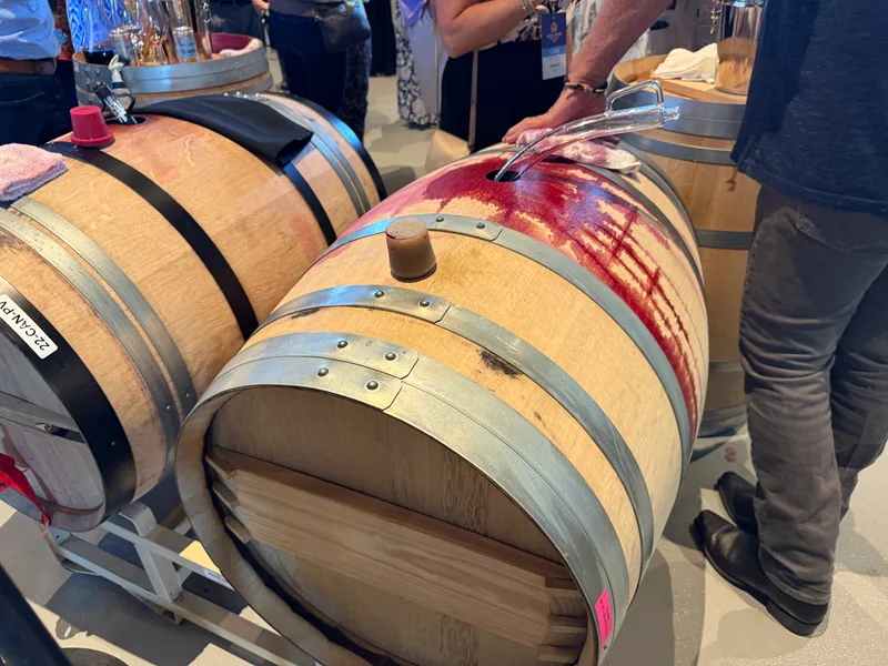 A host draws red wine from an oak barrel with a glass wine thief