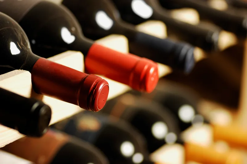 Wine bottles with red and dark capsules resting in a wooden rack