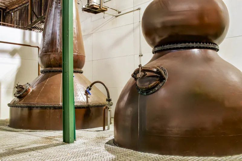 Two copper pot stills inside a bright still house