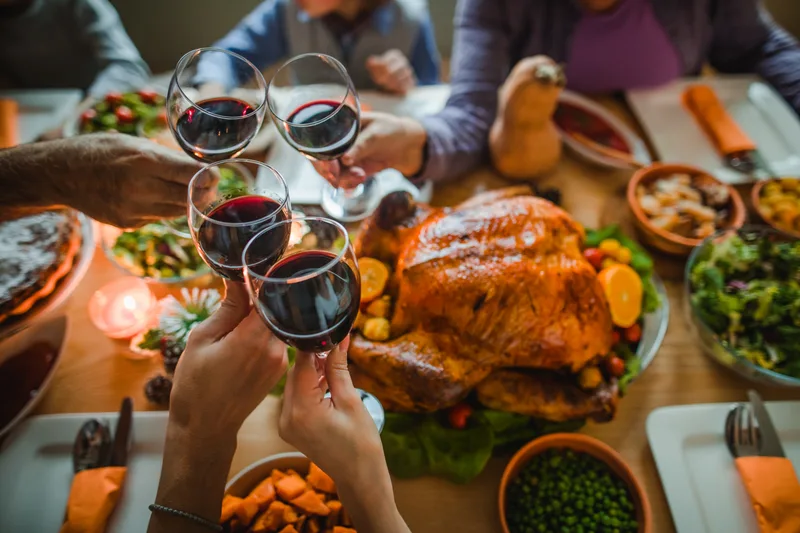 Friends raise glasses of red wine over a long autumn supper table