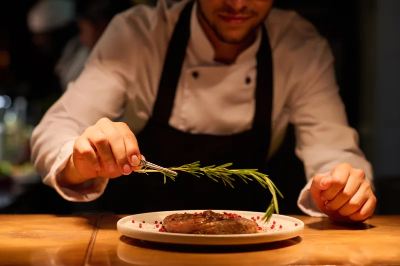 Chef placing a sprig of herbs on a plated roast
