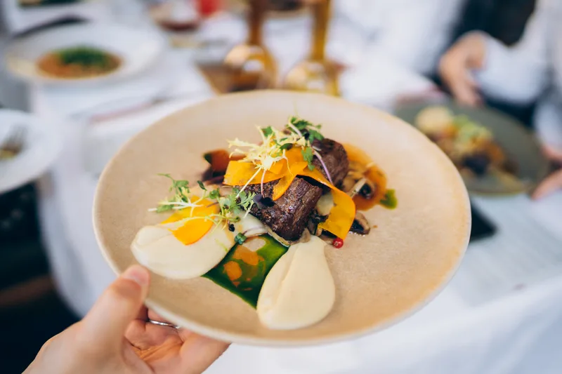 A plated main course with seared meat and a bright garnish held up at an event