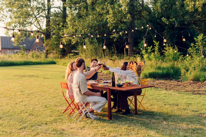 Friends raising glasses at an outdoor dinner in a field at golden hour