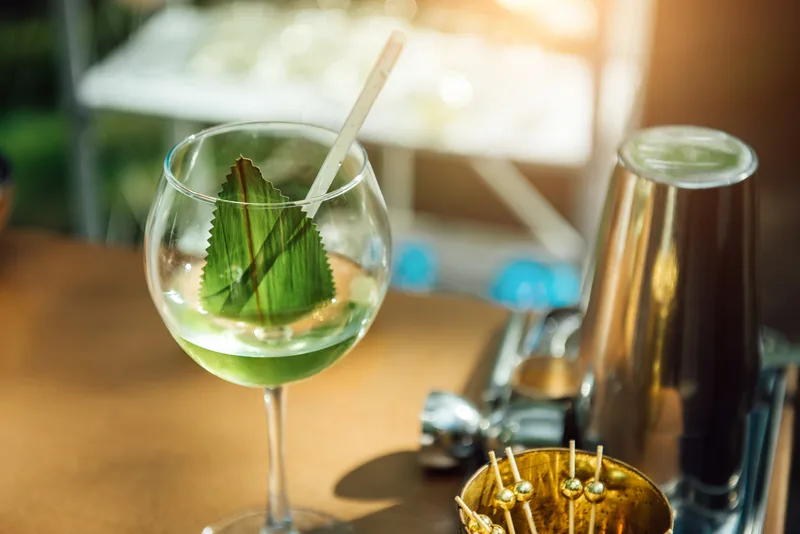 A green zero-proof spritz with a large basil leaf in a wine glass on a sunny bar