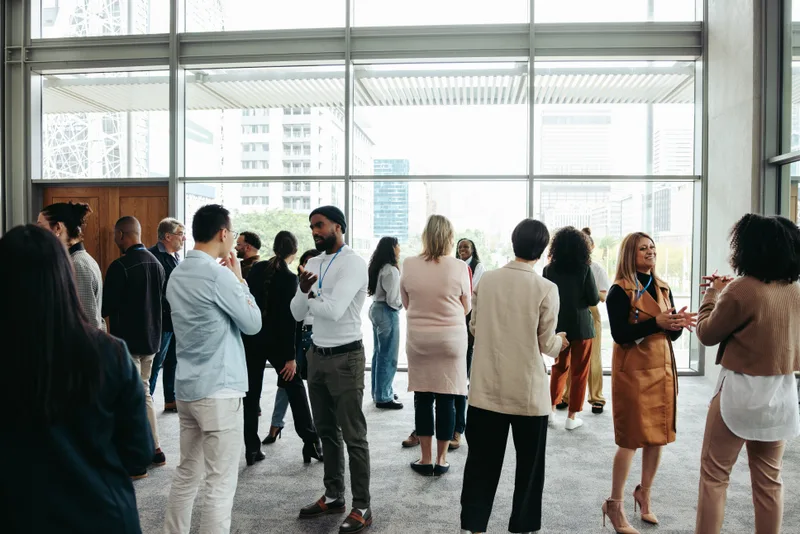 Colleagues talking in small groups at a bright office event with tall windows