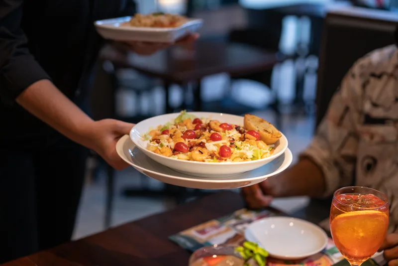 Server setting a plate of pasta in front of a guest