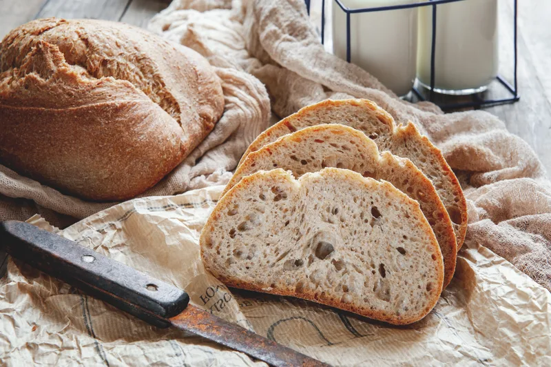 A rustic country loaf and thick-cut slices on a linen cloth beside a worn bread knife