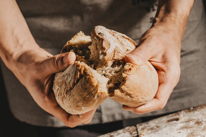 Two hands tearing open a crusty roll to show the soft, open crumb inside