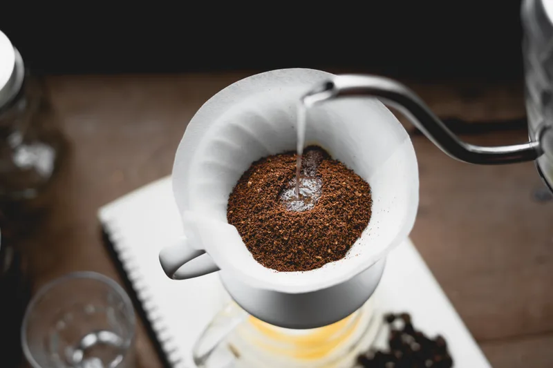 Hot water poured from a gooseneck kettle into a ceramic pour-over brewer full of fresh coffee grounds