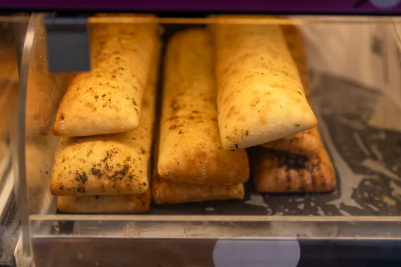 Herbed focaccia sticks stacked in a café display case, baked for a wholesale sandwich program