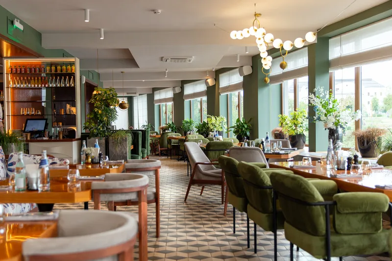 A bright dining room with green banquettes, round tables and big front windows