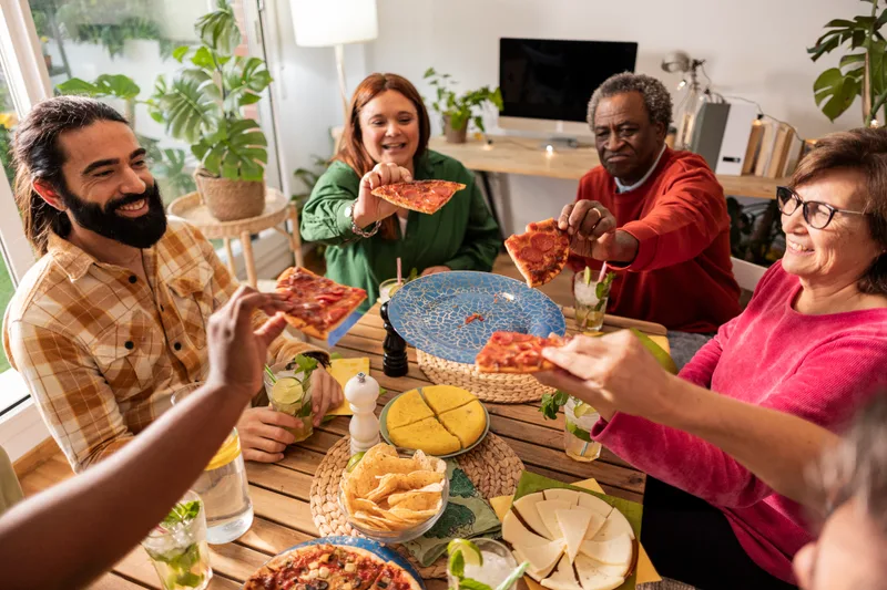 A family and friends of three generations passing pizza slices around a full table