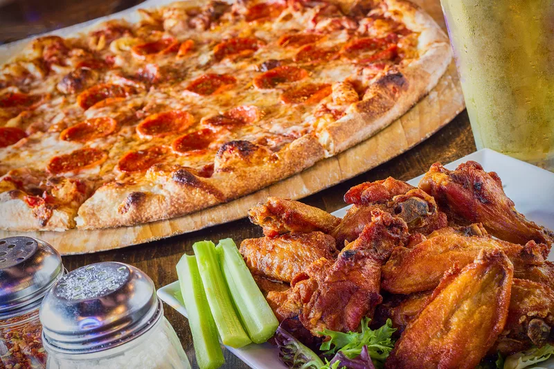 A large pepperoni pizza beside a plate of saucy chicken wings and celery sticks