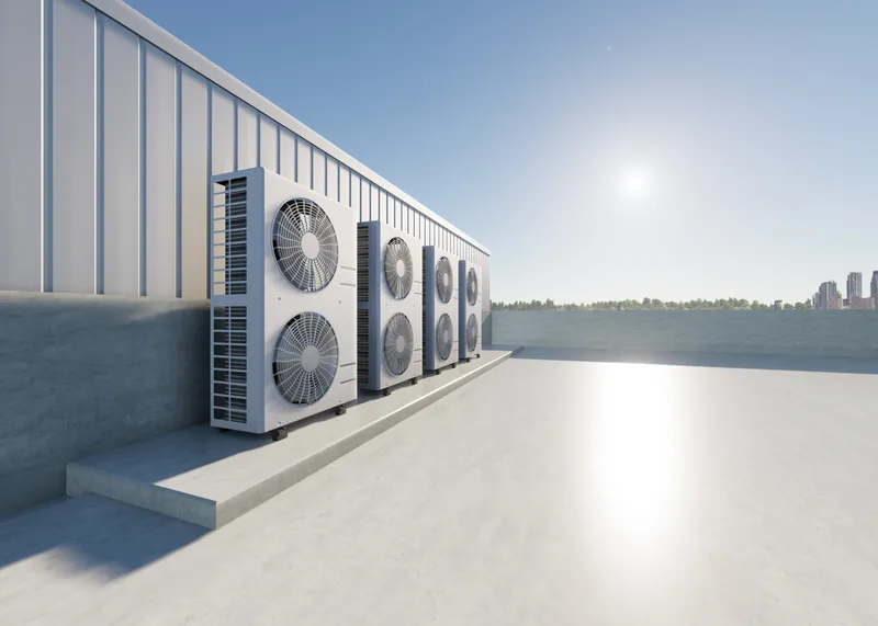 A row of air-conditioning condenser units mounted along a building's rooftop wall under a clear sky