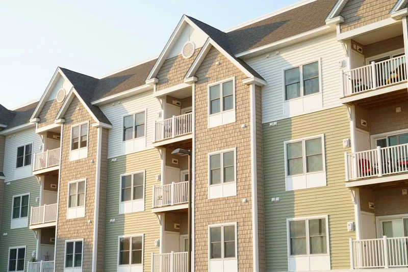 A garden-style apartment community with sage and cream siding, balconies, and a blue sky