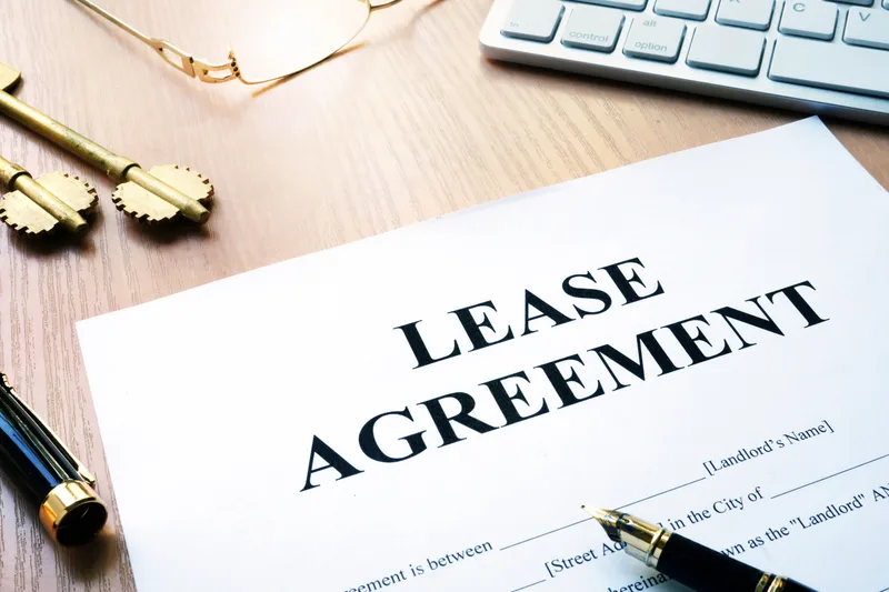 A printed residential lease agreement on a wooden desk with a pen, two brass keys and a keyboard