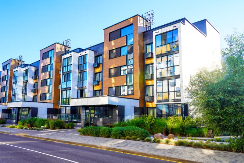 A modern mid-rise apartment building with orange and white panels and street trees out front